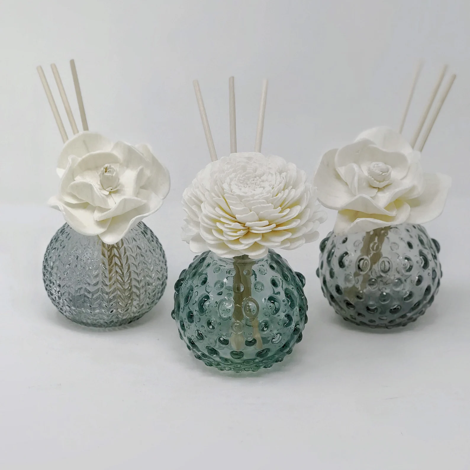 three blue, spherical, textured vases with white flowers and diffuser sticks