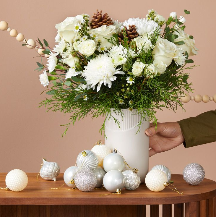 hand holding white vase of flowers with ornaments on the table